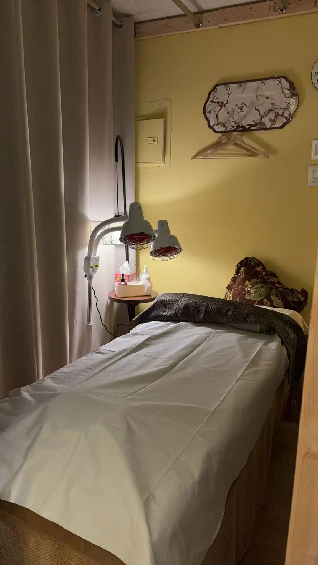 Private treatment room at U Beauty & Foot Spa with a freshly made massage bed, twin infrared heat lamps on a stand and a floral wall panel above the headrest